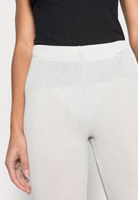 Leggings brancos perfurados com um ajuste justo e uma cintura elástica, apresentando uma superfície texturizada e bordas suaves.