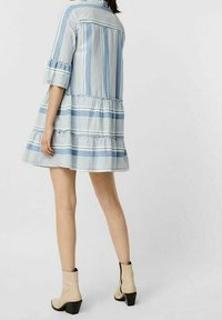 Rento denim-mekko, jossa on kermanväriset raidat ja röyhelöhelma. Mekossa on sinivalkoiset raidat, kolme neljänneskappaletta hihat ja istuva vartalo. Yhdistetty beigeihin nilkkabootseihin.