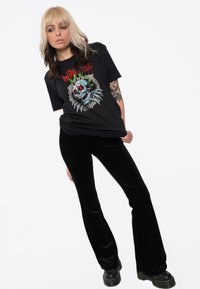 Black graphic t-shirt featuring a skull design with claws, worn with black velvet flared pants and chunky black boots.