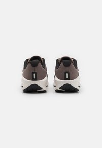 Laufschuhe mit einem strukturierten braunen Mesh-Obermaterial, schwarzen Akzenten und weißen Zwischensohlen. Verfügt über eine Lasche an der Ferse und eine gemusterte schwarze Außensohle.