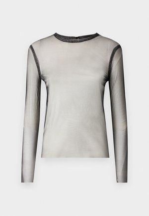 Top en maille noire à manches longues superposé sur un crop top noir uni, associé à un pantalon large noir taille haute. Escarpins noirs pointus et sac à main.