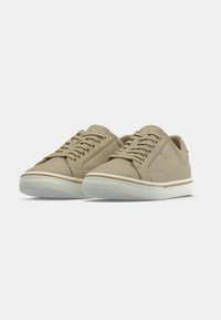 Paire de baskets beiges décontractées avec semelles en caoutchouc blanc et lacets, affichées sur un fond clair uni.