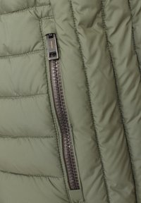 Grüne gepolsterte Jacke mit einer Reißverschlusstasche. Der Stoff ist glatt und zeigt eine horizontale Naht sowie einen schwarzen Reißverschluss mit einem orangen Zugband.