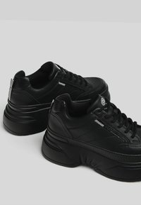 Svarta plattformssneakers i läder med texturerade detaljer, rund tå, snörning och mönstrad dekoration på sidorna och hälen.
