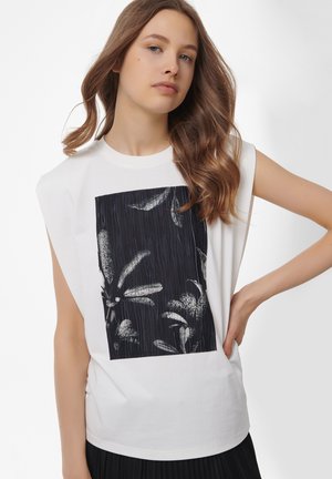 Top en coton sans manches de couleur blanche avec un imprimé graphique sombre et des motifs floraux. Coupe droite avec une coupe décontractée. Texture lisse.