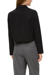 Czarna krótka kurtka z długimi rękawami, z klasycznym kołnierzem. Nosi ją się na szare dopasowane spodnie o gładkiej teksturze i subtelnym wzorze.