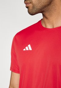 Punane sportlik T-särk lühikeste varrukatega, ümara kaelusega, siledast materjalist, vasakul õlal kolmnurkse mustriga valge logoga.