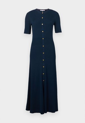 Marineblå ribbestrikket kjole med korte ermer, rund hals og gullknapper foran. Kjolen har en utsvingt skjørt som når midt på leggen.