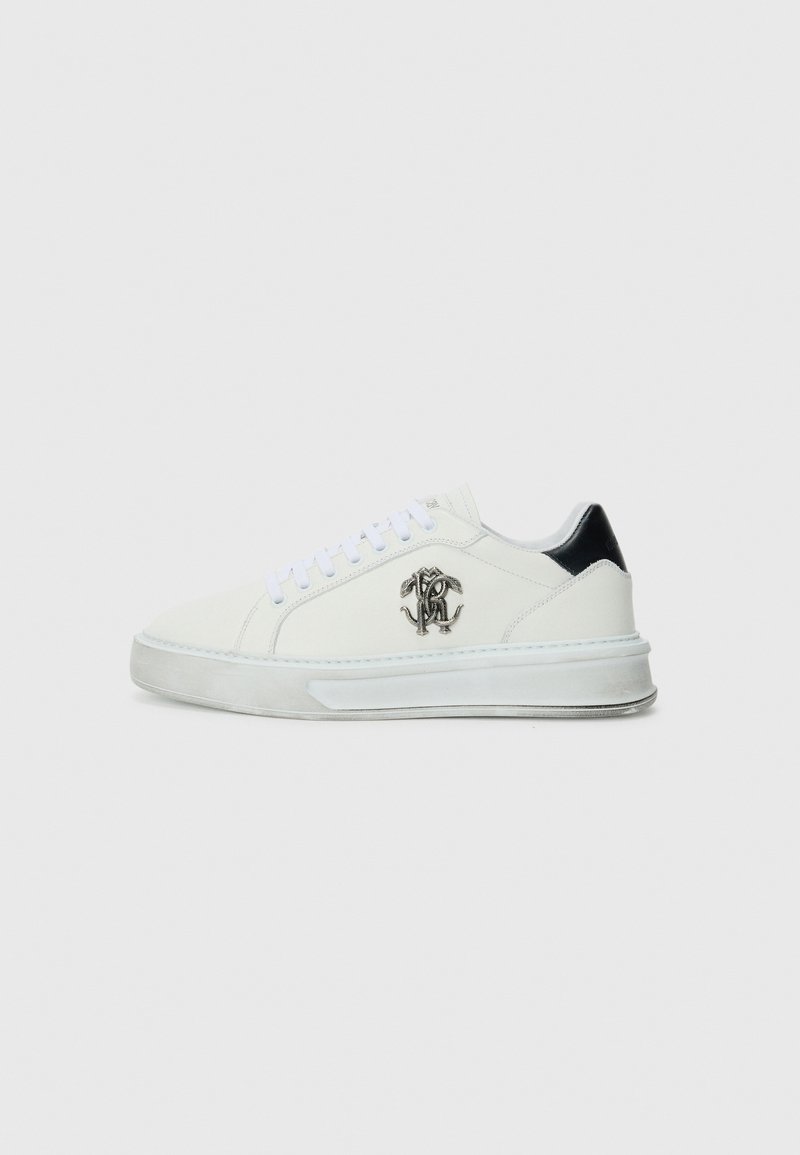 Sneakers bianchi in pelle con un accento nero sul tallone, punta rotonda, suola piatta e un dettaglio del logo testurizzato sul lato. I lacci sono bianchi.