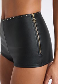 Shorts noirs en cuir taille haute avec une fermeture éclair dorée sur le côté et des clous dorés le long de la taille. Texture lisse.