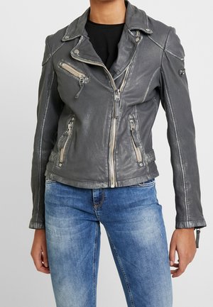 Person wearing a gray leather biker jacket with multiple front zippers over a black shirt, paired with blue faded jeans.