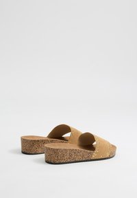Sandalias de plataforma marrones con suela de corcho, parte superior de ante, dos correas anchas decoradas con pequeños remaches de metal. Diseño con punta redondeada y parte trasera abierta.