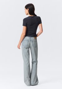 Schwarzes, eng anliegendes T-Shirt kombiniert mit hellblauen, ausgestellten Jeans, die einen braunen Lederpatch und klassische Gesäßtaschen aufweisen. Glatter Stoff und lockerer Schnitt.