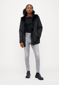 Sort hættejakke med en faux fur-foring, parret med en ribbet sort top og lysegrå skinny jeans. Sorte ankelstøvler fuldender outfittet.