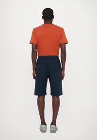T-shirt orange à manches courtes et shorts bleu marine. Les shorts ont une taille élastique et deux poches arrière. Le footwear est des baskets gris clair.