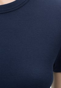 Laivastonsininen ribbineulottu lyhythihainen paita, jossa on pyöreä pääntie, kuvattuna ylävartalosta hartia-alueelle.