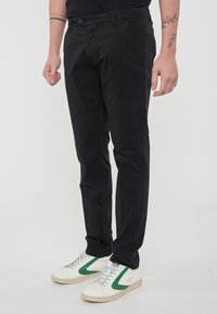 Pantaloni in cotone neri con design a gamba dritta, caratterizzati da una chiusura frontale con bottone e tasche laterali, abbinati a sneaker bianche e verdi.