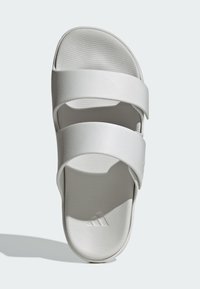 Valkoinen liukusandaali, jossa on kaksi leveää remmiä, litteä pohja, kuvioitu pohjallinen ja hienovarainen logodetalji sisäpohjassa. Sileä, synteettinen materiaali.