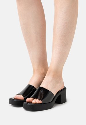 Sorte platformsandaler med en blank, gennemsigtig rem, åbent tå-design og tekstureret sort sål. Enkel blokhæl.