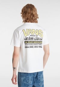 Bílá bavlněná tričko s žlutým a černým grafickým potiskem na zadní straně, který zahrnuje logo "VANS" a kontaktní údaje.