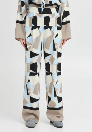 Høj talje, vide ben bukser med abstrakte beige, sorte, lyseblå og hvide geometriske mønstre, båret med grå loafers.
