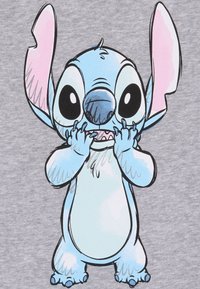Personaggio dei cartoni animati Stitch con grandi orecchie rosa, pelo blu e occhi grandi, visualizzato su uno sfondo grigio. Il personaggio appare giocoso ed eccitato.