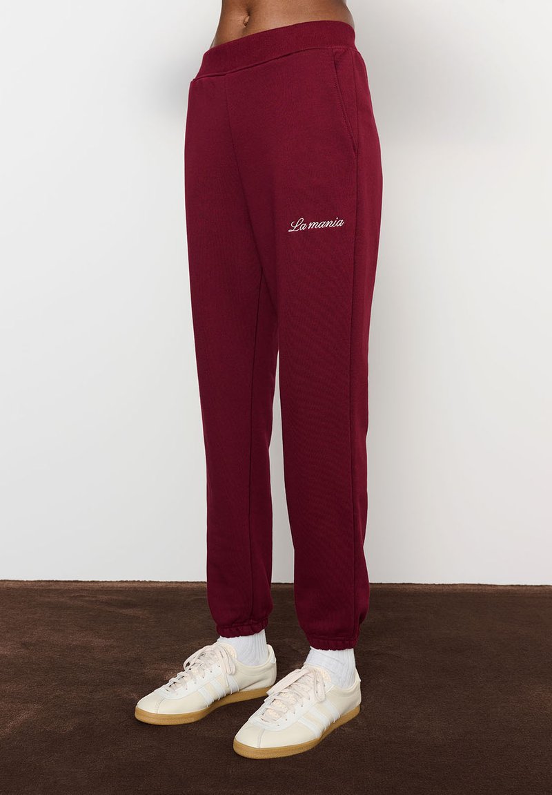 Burgundiški sportiniai kelniukai su elastingu juosmeniu ir šonkaulio rankovėmis, su balta siuvinėta "La mania" kairėje pusėje.