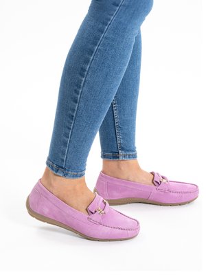 Person wearing blue skinny jeans and pink suede loafers with gold buckles, standing against a white background.