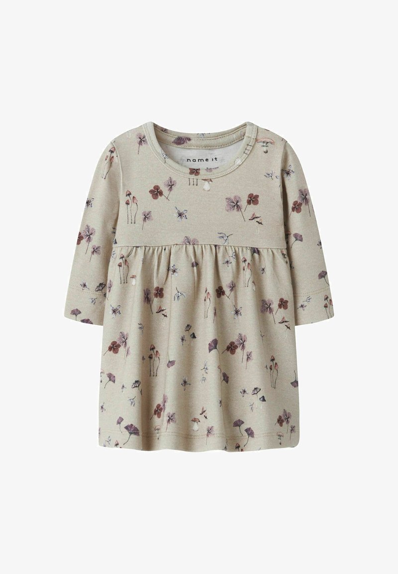 Haut long beige clair avec taille froncée, arborant un motif floral dans des teintes de violet, de marron et de vert. Tissu en coton doux.