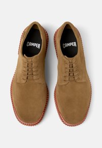 Scarpe in suede marrone con suola in gomma e design con lacci, con una fodera interna nera e il nome del brand "CAMPER" visibile.