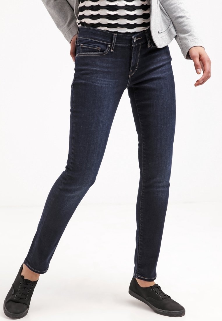 Jean slim bleu foncé en denim, doté de cinq poches, passants de ceinture et surpiqûres contrastées. Porté avec un haut rayé et des baskets noires.