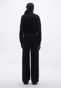 Fekete magas nyakú pulóver széles szárú fekete nadrággal párosítva. Sima textúra és laza szabás. Minimalista dizájn, látható minták nélkül.