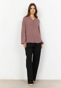 Red-patterned long-sleeve blouse with a v-neck and three buttons, paired with black straight-leg trousers and nude high-heeled shoes.