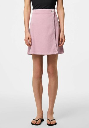 Kvinde iført en lyserød A-formet slå-om-nederdel med knapper foran, kombineret med sorte flip-flops og en sort top.