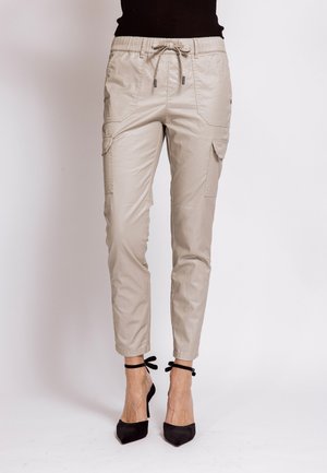 Beige cargo pants with drawstring waist and flap pockets worn with black ankle-tie high heels.