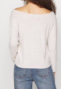 Haut beige clair à épaules dénudées avec manches longues, en tissu doux, associé à un jean taille haute avec poches arrière.