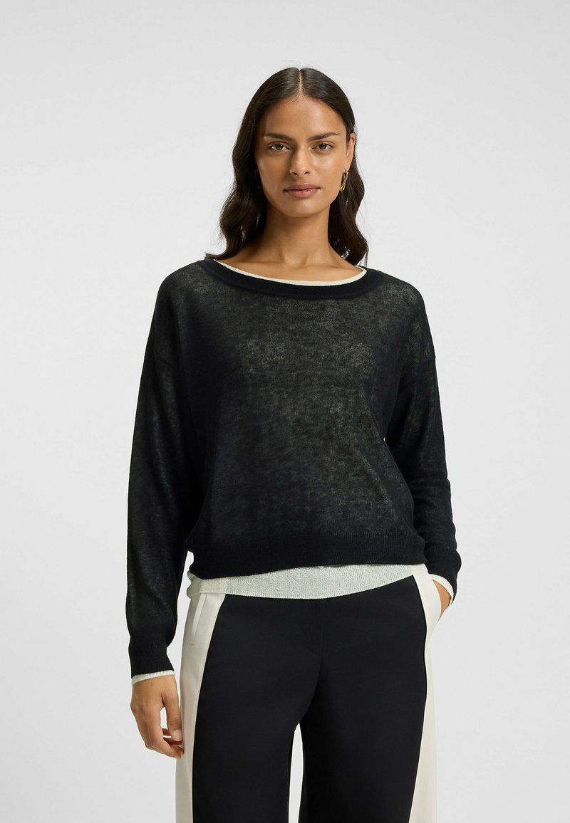 Black, lightweight, loose-fitting sweater with a boat neck, layered over a white textured top. Long sleeves and subtle transparency.