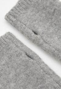 Materialul tricotat gri are o textură moale, având detalii cu un gol și o buclă vizibilă. Marginea este finisată, sugerând uzură sau o caracteristică de design.