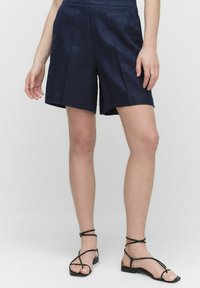 Tummansinisiä lyhyitä housuja, jotka on valmistettu kevyestä kankaasta. Niissä on sivutaskut, rento malli ja hienovaraiset taitteet lisäämässä yksityiskohtia.