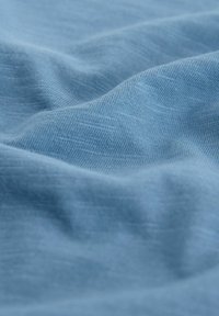 Light blue fabric with soft, textured surface, displaying gentle waves and folds. The weave is fine, giving a smooth appearance.