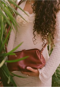 Bolso de mano de cuero rojo con una textura suave, enmarcado con una correa de herrajes dorados. El bolso tiene bordes redondeados y un cierre de broche.