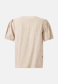 Chemise beige à manches courtes avec manches bouffantes et tissu texturé vue de dos sur un fond uni.