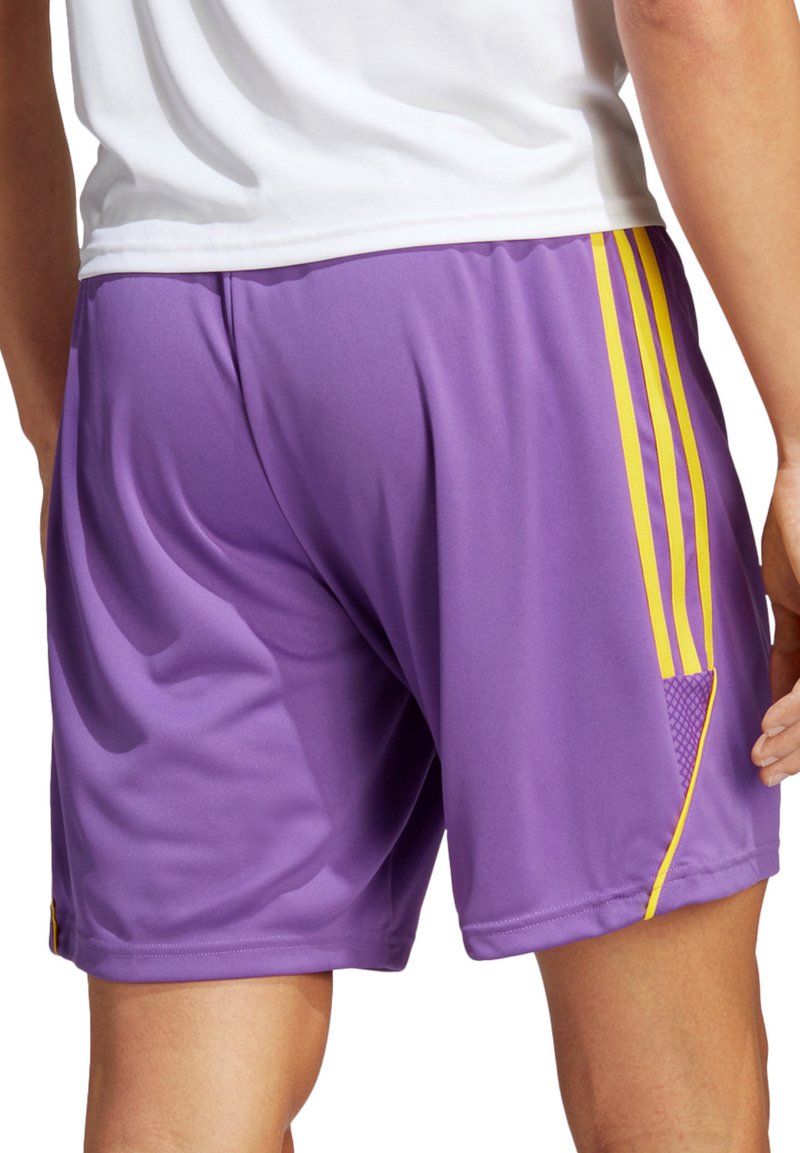 Paarse sportshorts van gladde stof, met gele zijstrepen en gekorrelde accenten aan de onderkant van de linkerzijde.