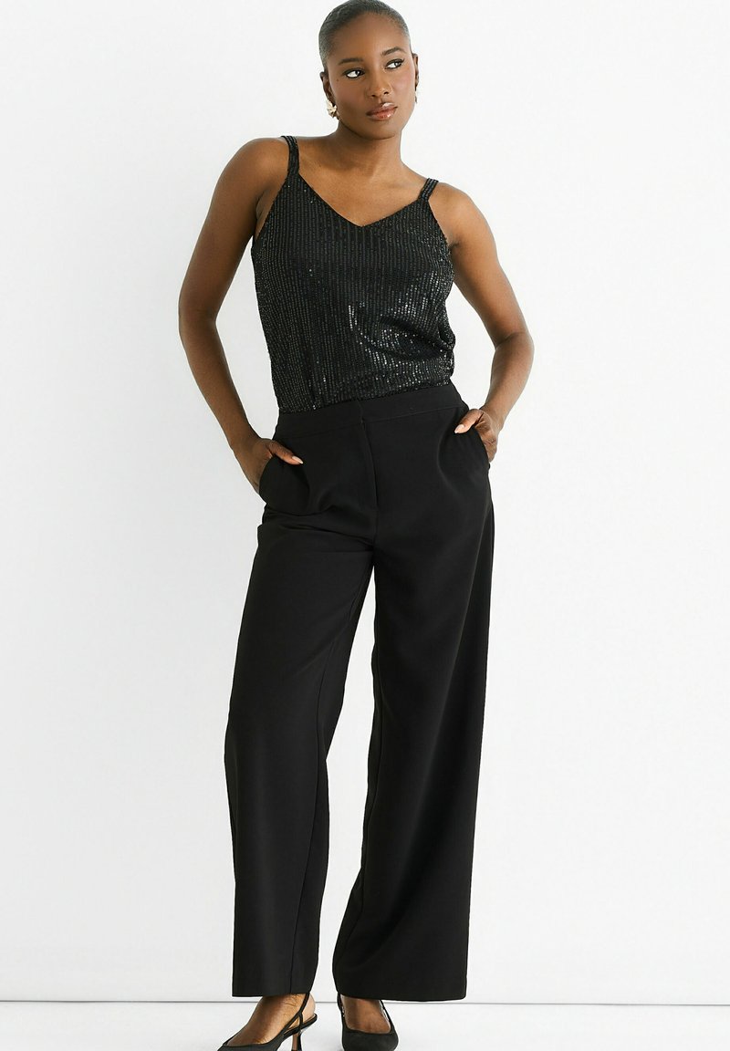 Black sequin cami top with adjustable straps paired with high-waisted black wide-leg trousers and black strappy heels.