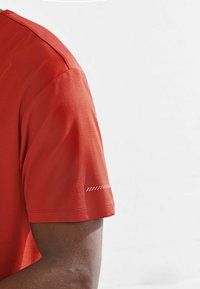 Rotes Sport-T-Shirt mit atmungsaktiver Netzstruktur, featuring kurze Ärmel und einem kleinen Streifendetail nahe dem Ärmelabschluss.