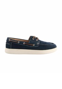 Chaussure bateau en daim bleu marine avec semelle blanche, lacet en cuir marron passé à travers des œillets métalliques, et détails de couture blancs.