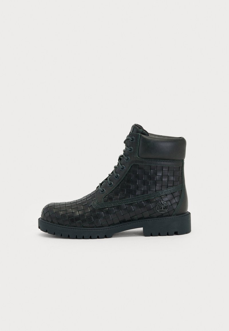 Black woven leather ankle boots with a sturdy rubber sole, featuring green accents and a logo on the side. Lace-up design.
