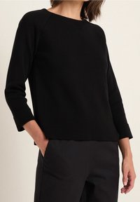 Svart stickad tröja med rund halsringning, trekvartsärmar och avslappnad passform. Strukturerat tyg med sprund i sidan vid fållen.
