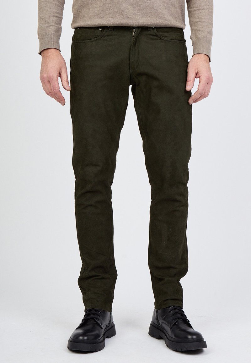 Oliivinvihreät mokkataskut, joissa on kapea leikkaus, vetoketjukiinnitys, viisi taskua ja sileä pinta, yhdistettynä mustiin nauhakengiin.