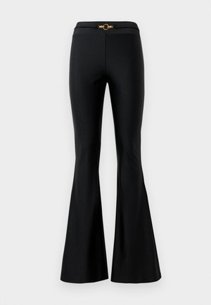 Pantalons évasés noirs avec une texture lisse, dotés d'une taille ajustée et d'un accent circulaire doré à l'avant. Fabriqués dans un matériau extensible.